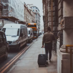man holding luggage walking near road during daytime