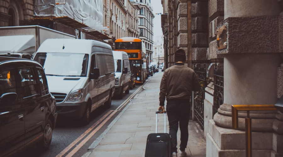 man holding luggage walking near road during daytime