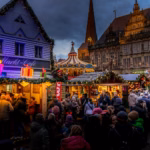 Crowds among the wooden stalls of a Christmas market in the evening