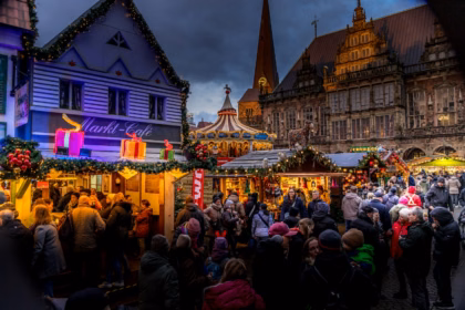 Crowds among the wooden stalls of a Christmas market in the evening