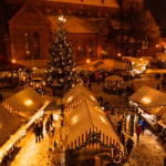 Lit-up Christmas market stalls in a historic town at night